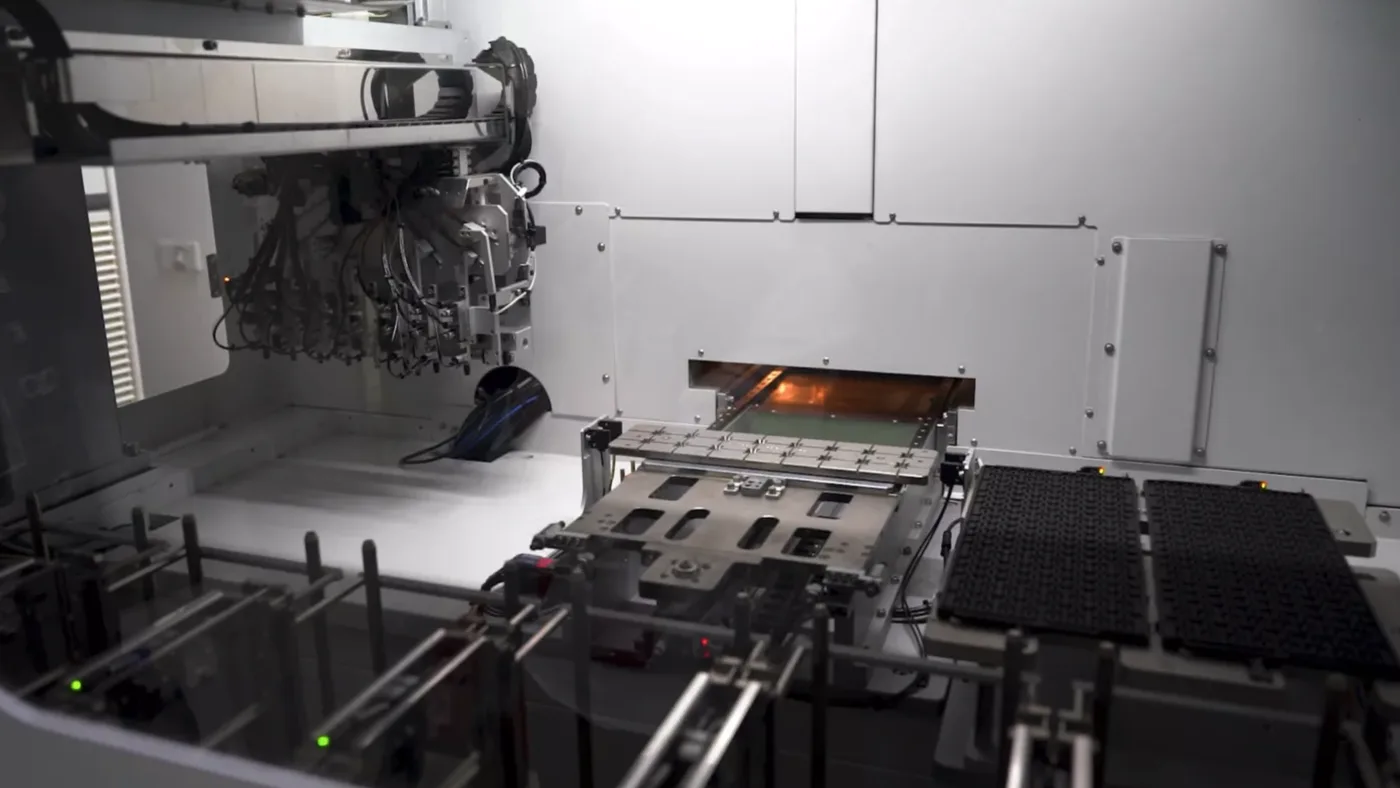 Inside a surface-mount machine: the placement head above a board, with the reflow oven opening behind it